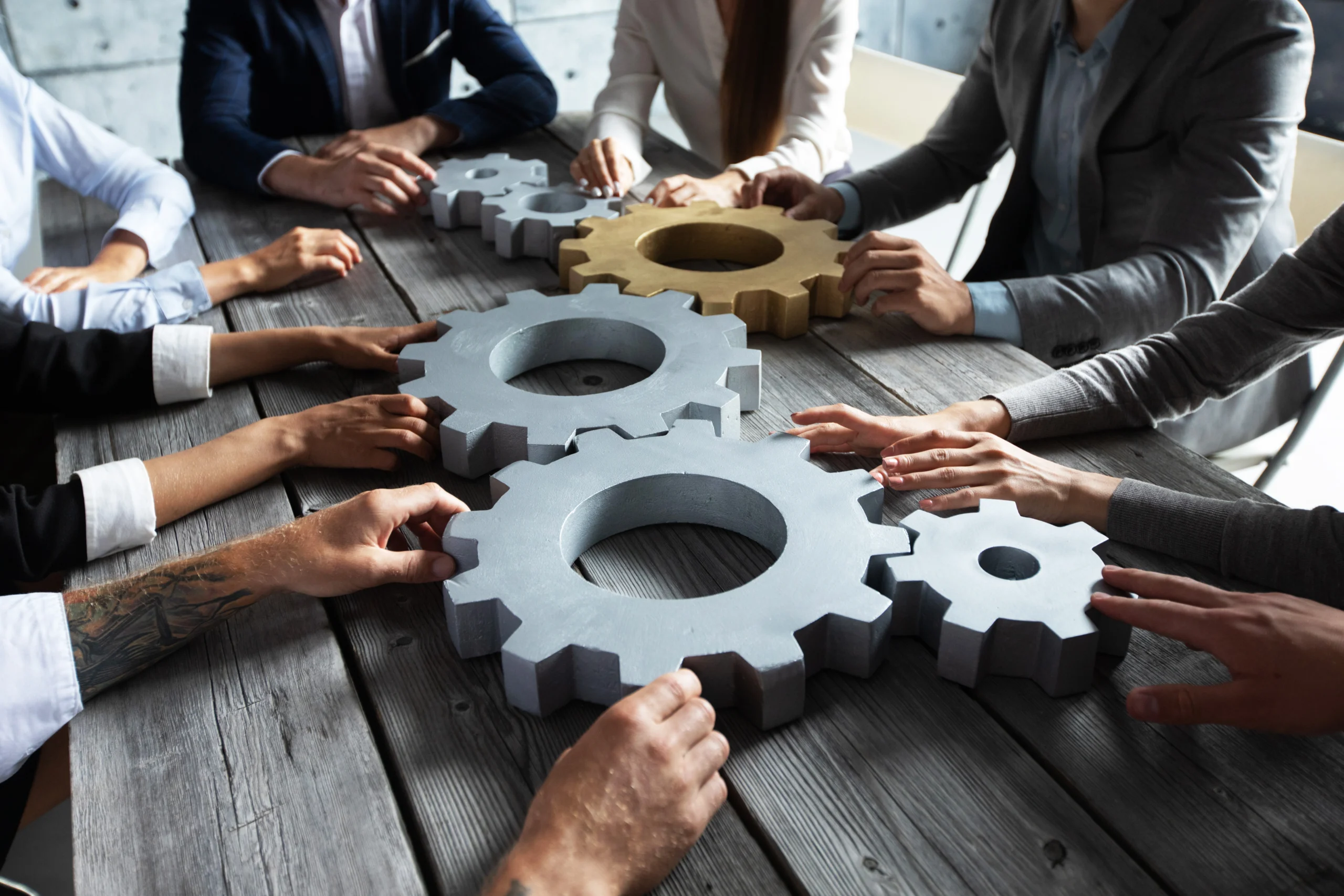 team around table holding gears symbolizing teamwork