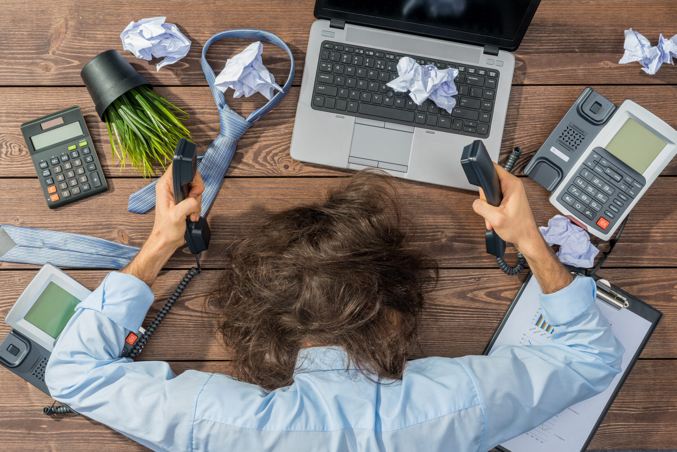 overworked person with head on desk surrounded by technology