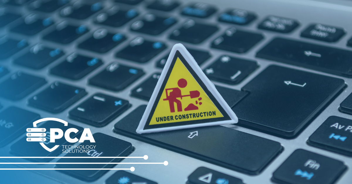 Yellow 'Under Construction' triangle sign rests on a laptop keyboard near the PCA Technology Solutions logo in the lower-left corner.